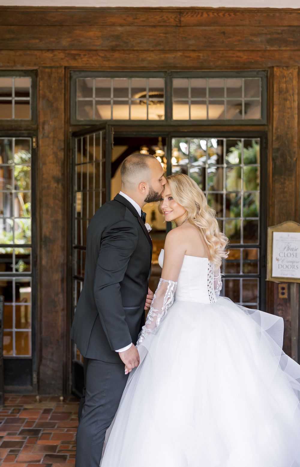 Romantic wedding couple embraces in front of rustic wooden doorway with glass panes.
