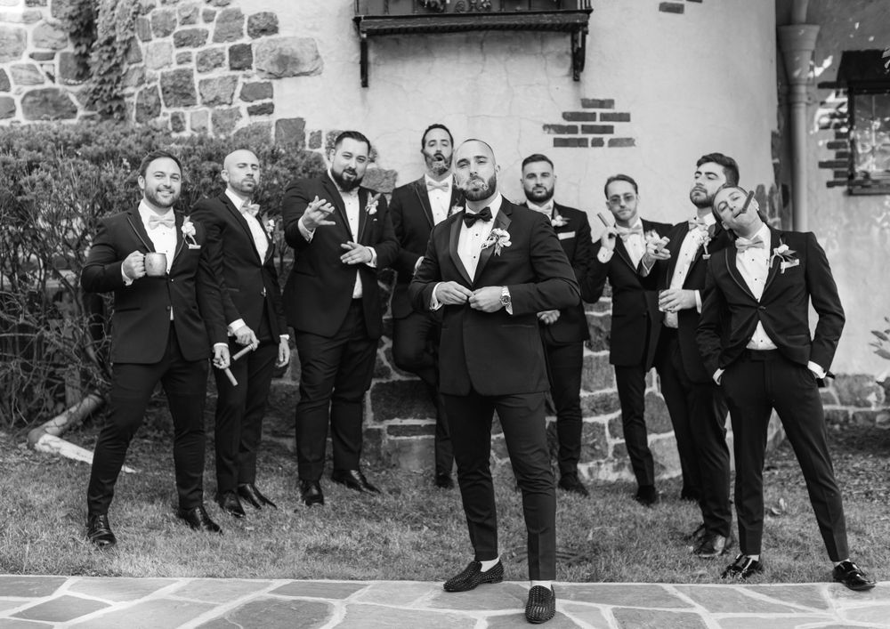 Black and white photo of groomsmen posing playfully outside stone building.