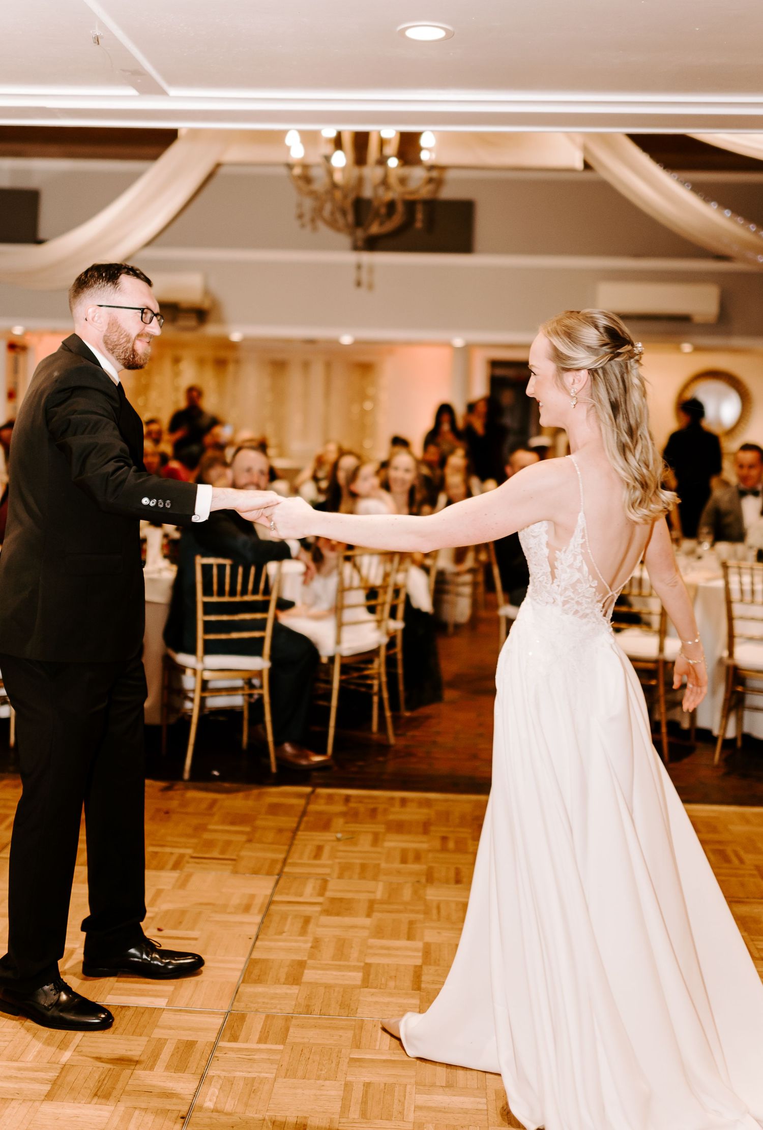 Newlyweds share a joyful dance moment on parquet flooring at their reception.