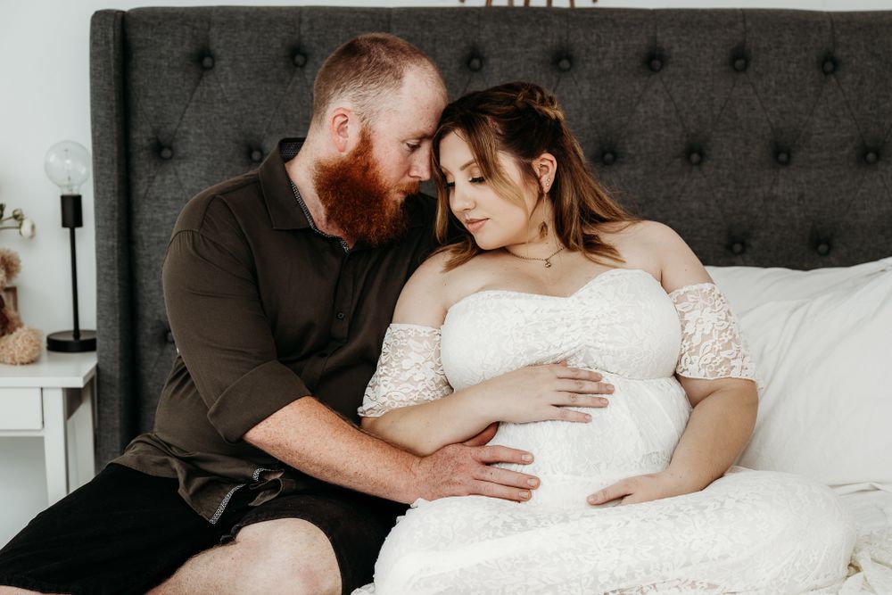 An intimate maternity moment on a gray tufted headboard in a bedroom setting.
