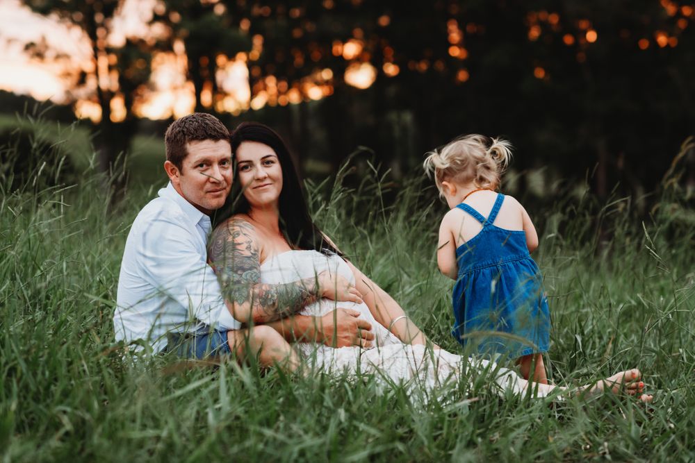 A family sits together in tall grass during golden hour sunset.