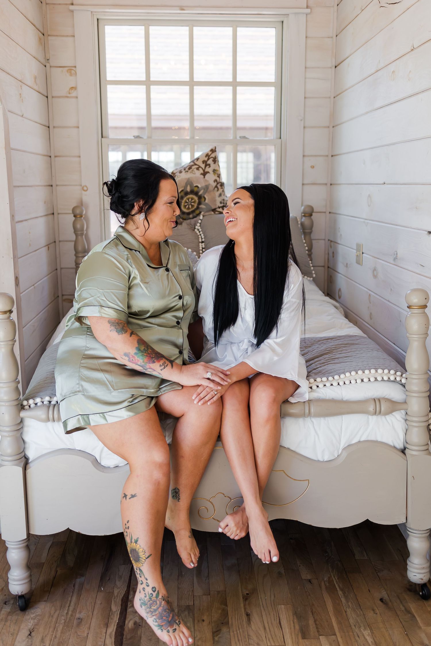 Two women share an intimate moment sitting together on a vintage white bench in a rustic room.