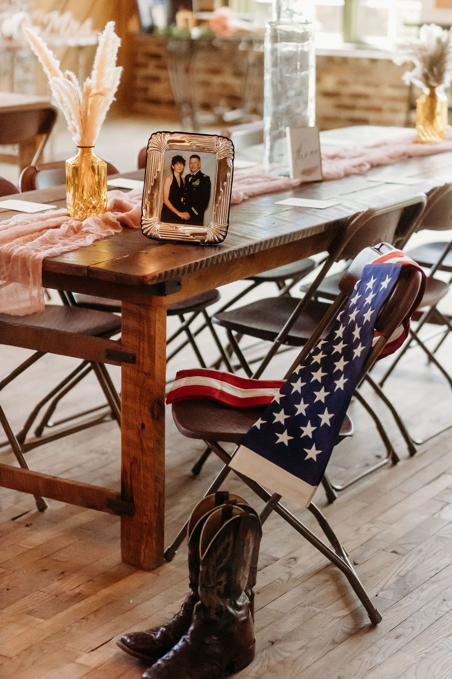 Rustic wedding reception table with American flag chair and cowboy boots beneath.