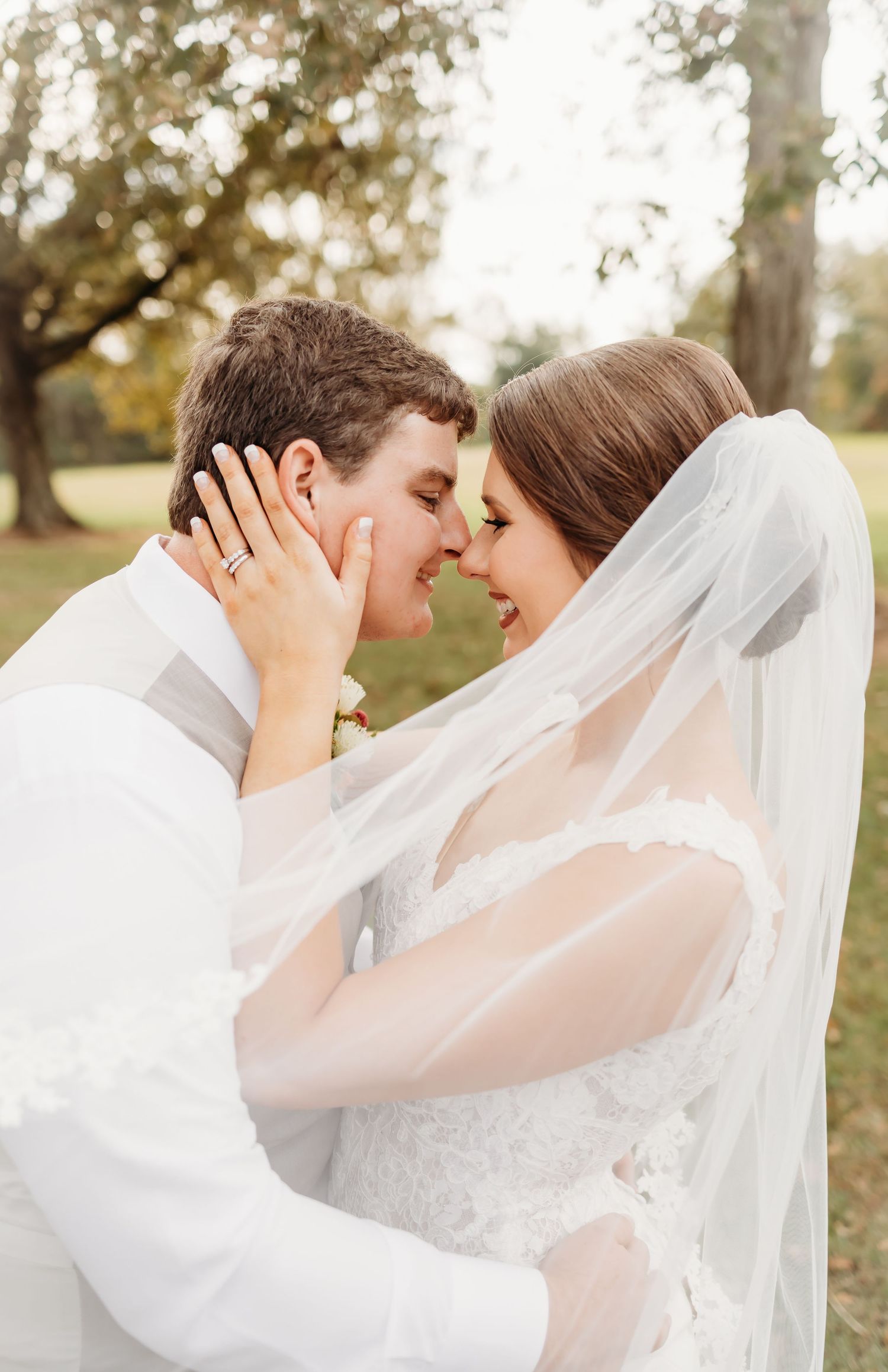 A romantic moment captured between a couple with a flowing white veil in an outdoor setting.