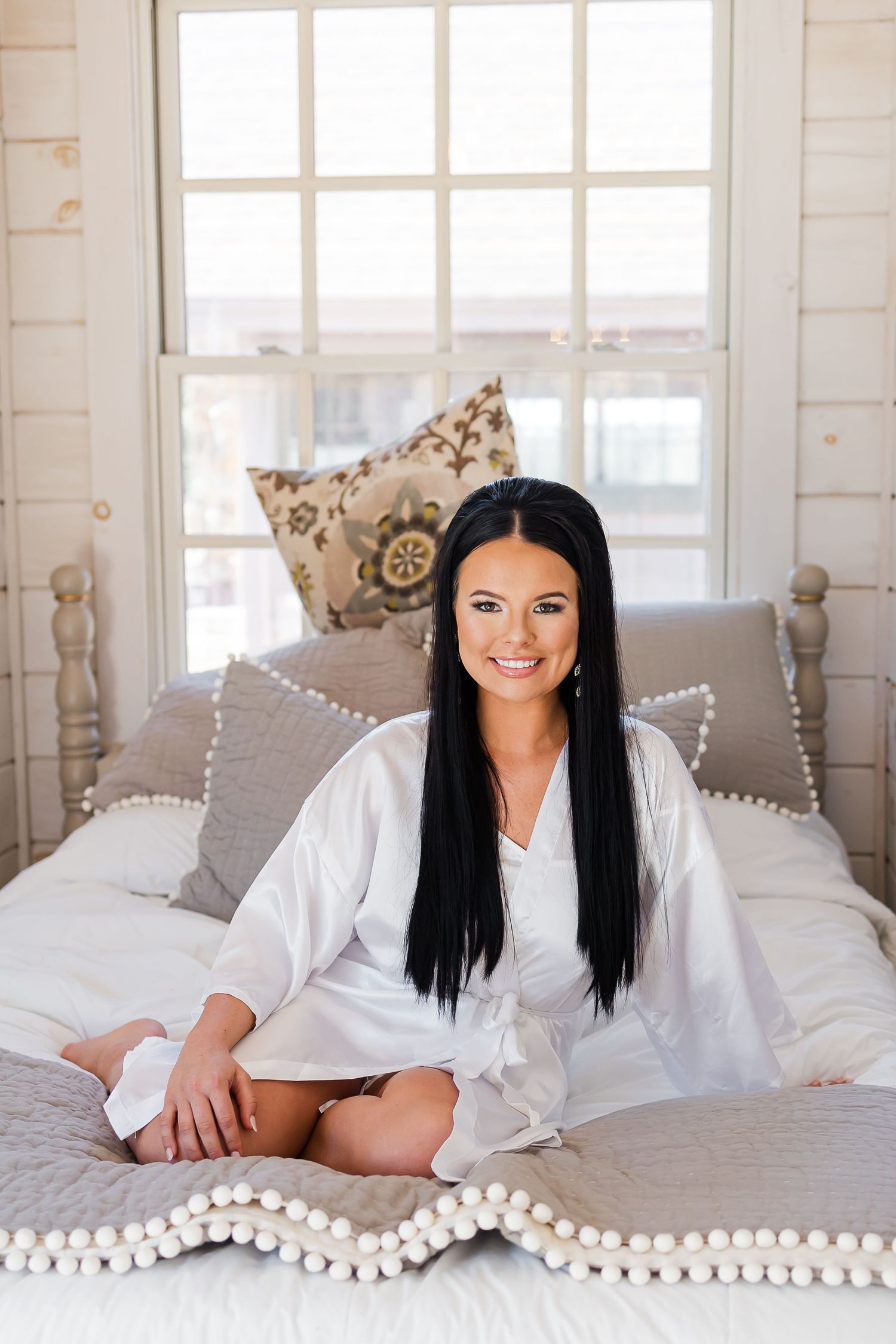 Bridal boudoir photo session on a white bed with decorative pillows.