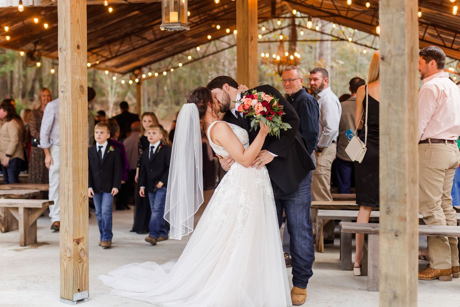 Wedding reception celebration in a rustic barn venue with string lights and wooden beams.