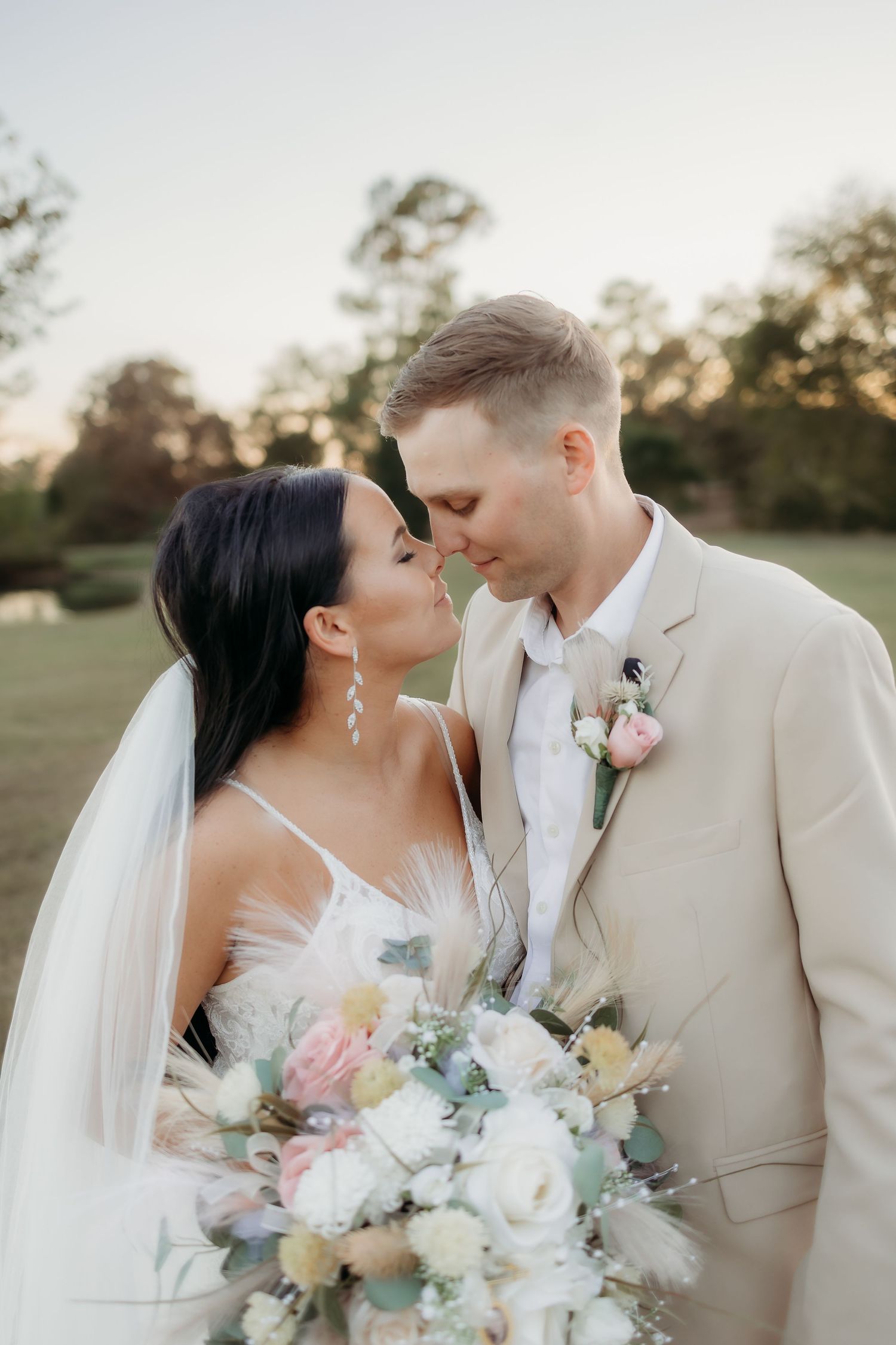 Newlyweds share intimate moments at sunset while holding pastel floral bouquet.