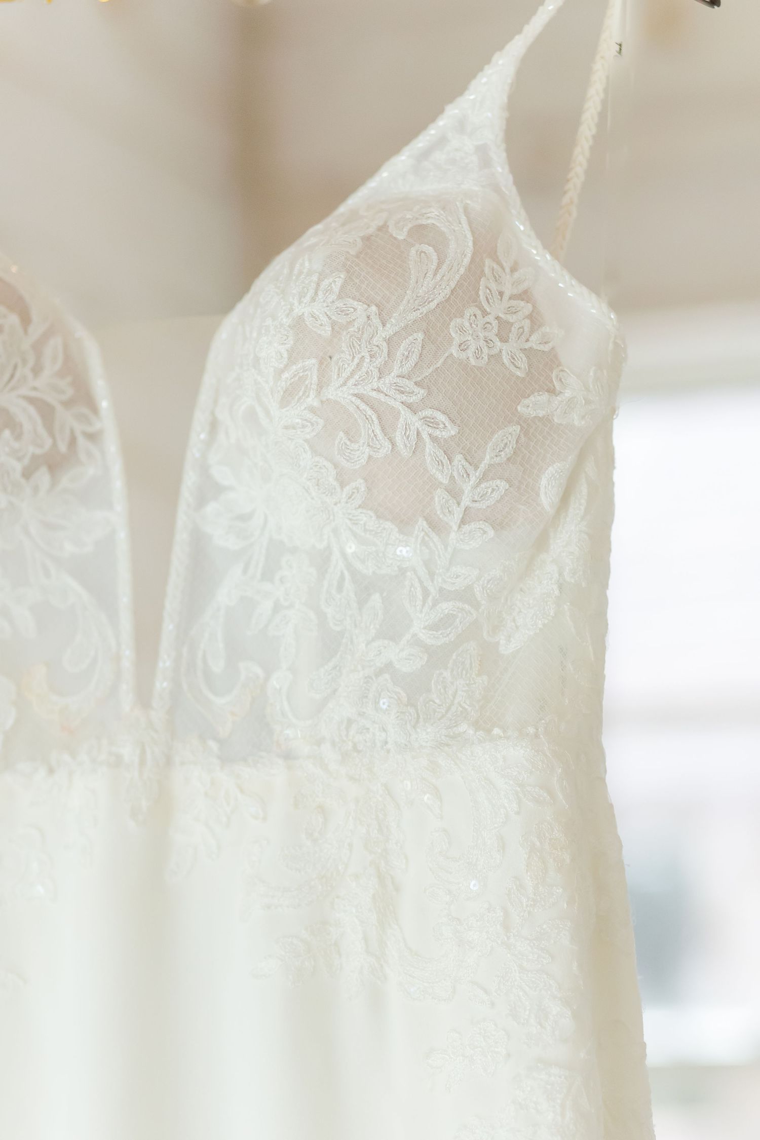 Close-up of delicate white lace wedding dresses hanging on display.