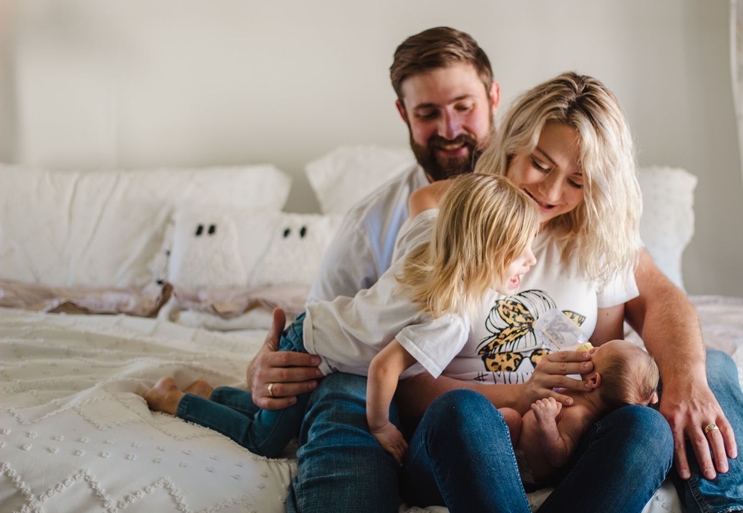 New parents holding celebrating newborn baby with toddler in their home.