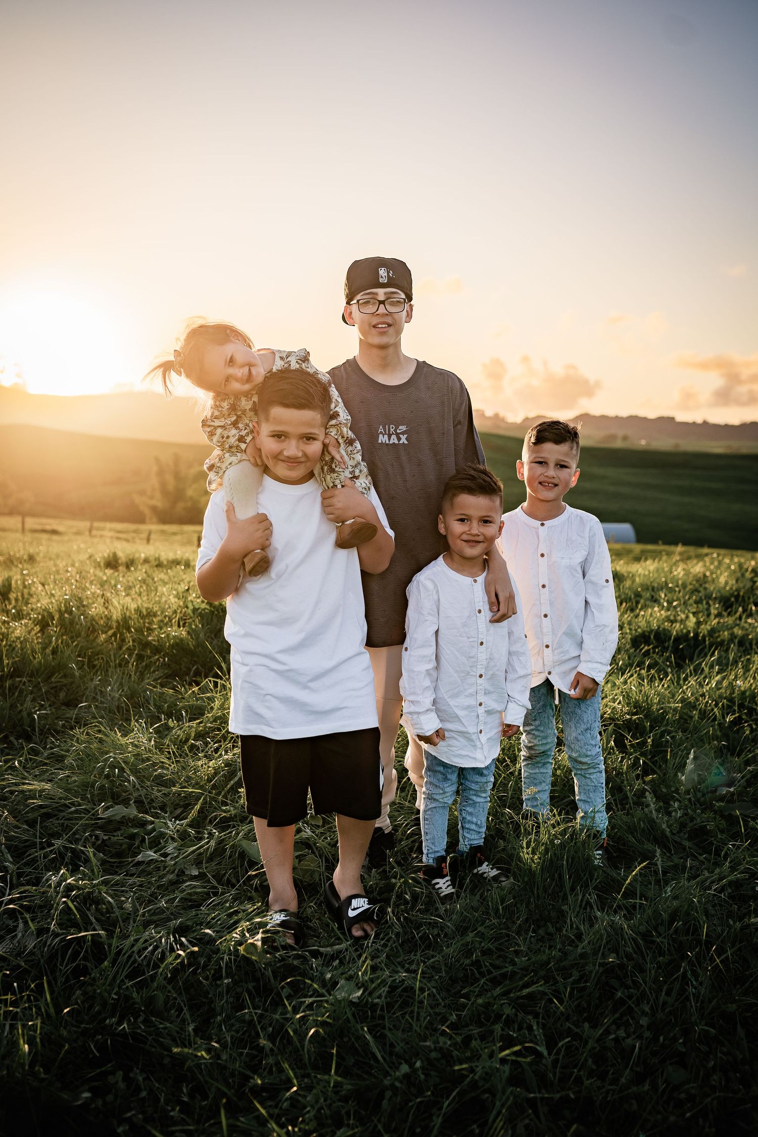 Group poses together in a grassy field at sunset with golden sunlight streaming through in the background.