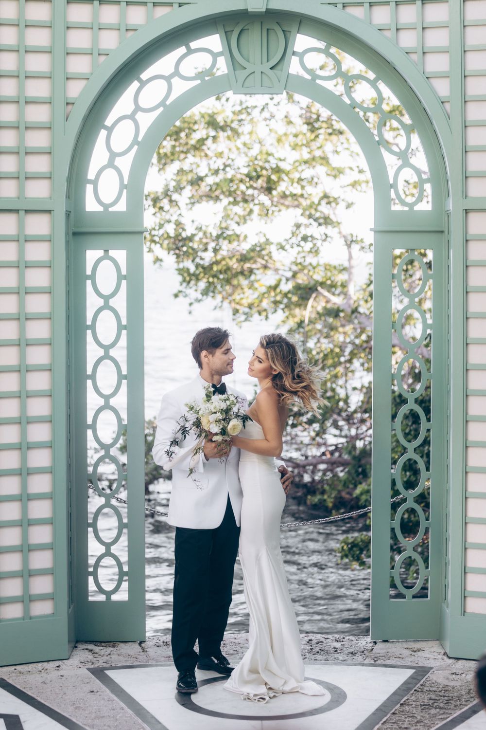Romantic wedding couple embracing under ornate mint green garden archway.
