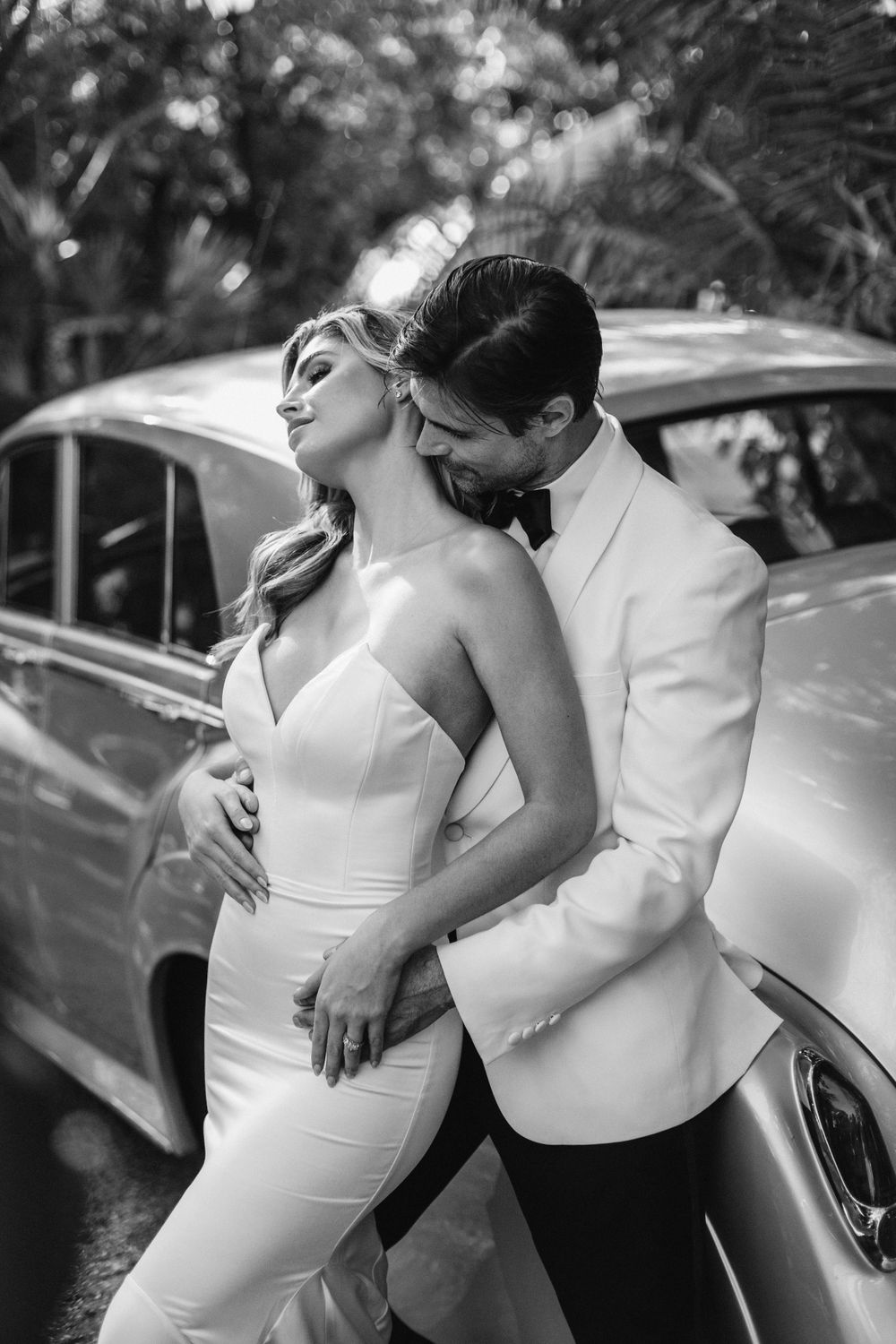 Intimate black and white portrait of couple against classic car.