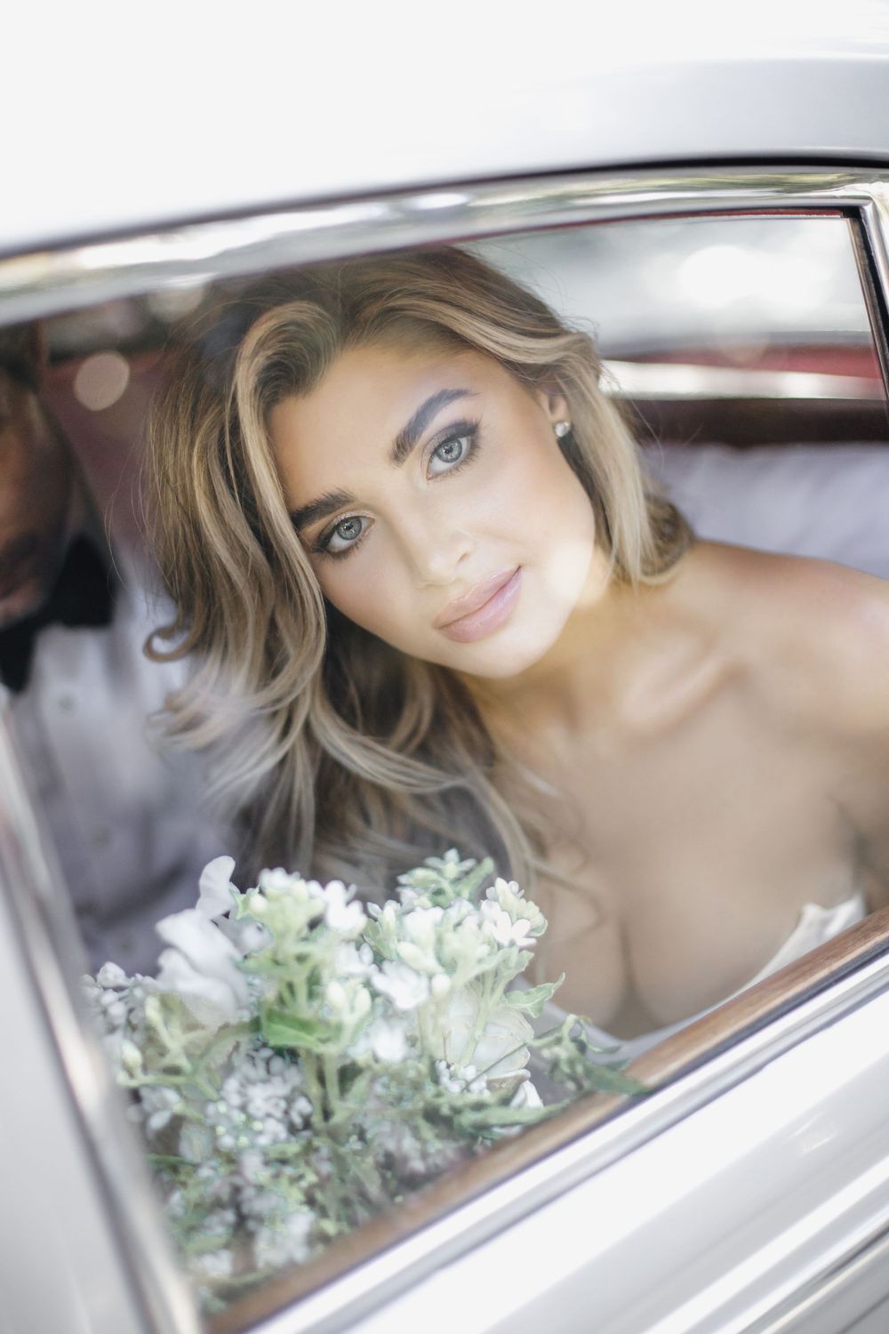 Classic bridal portrait through vintage car window with soft white bouquet.