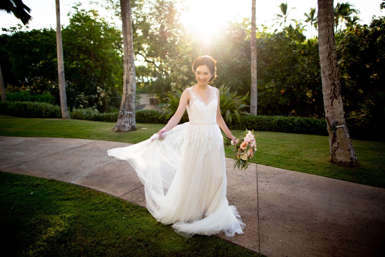 A flowing white wedding dress catches the sunlight in a lush garden setting with palm trees.