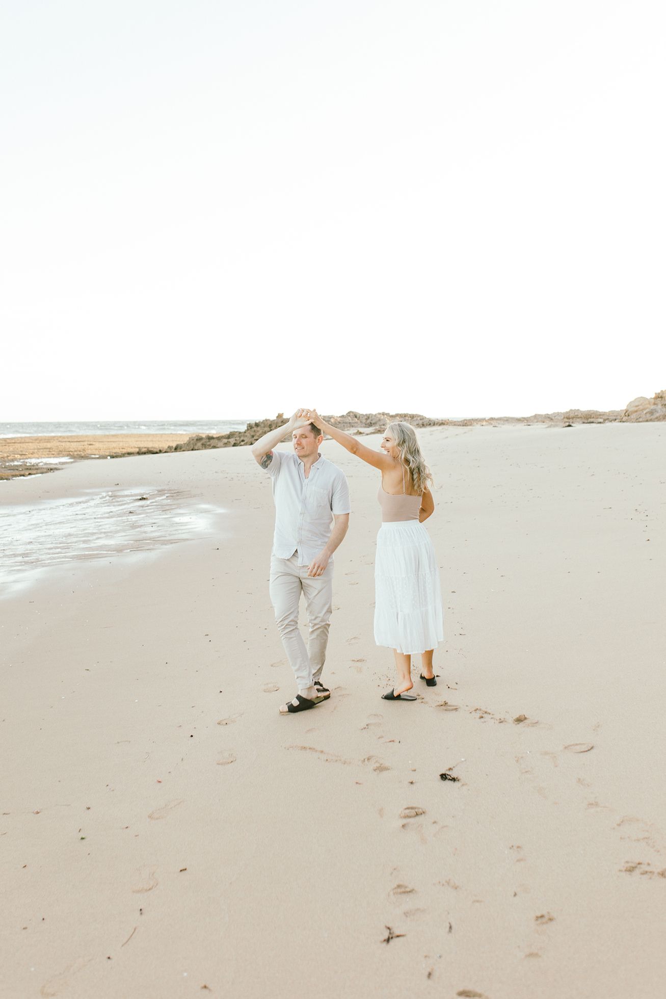 Pair dancing together on an empty beach with coastal cliffs in the distance.