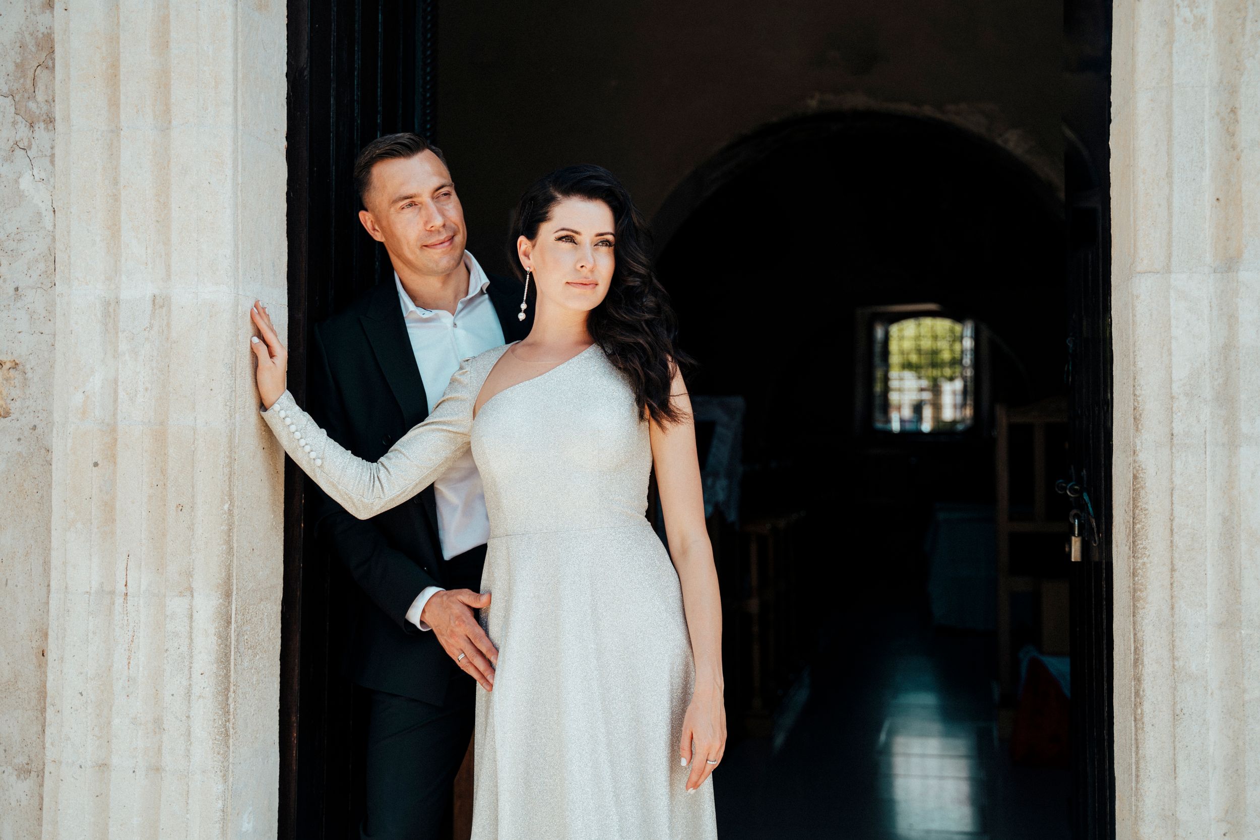 Artistic wedding portrait of couple posing in doorway of stone building.
