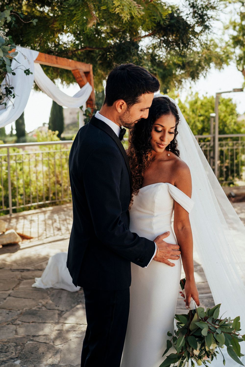 Couple embraces under floral wedding arch during romantic outdoor ceremony.