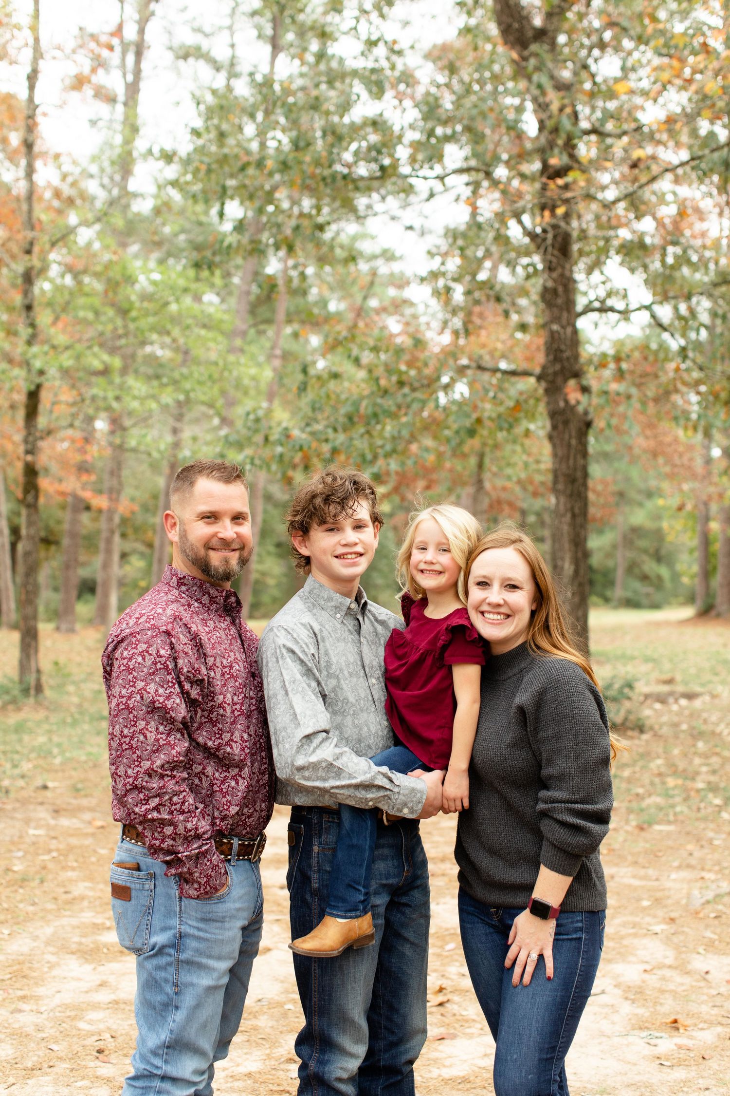 A loving family portrait captured outdoors among autumn trees on a natural trail.