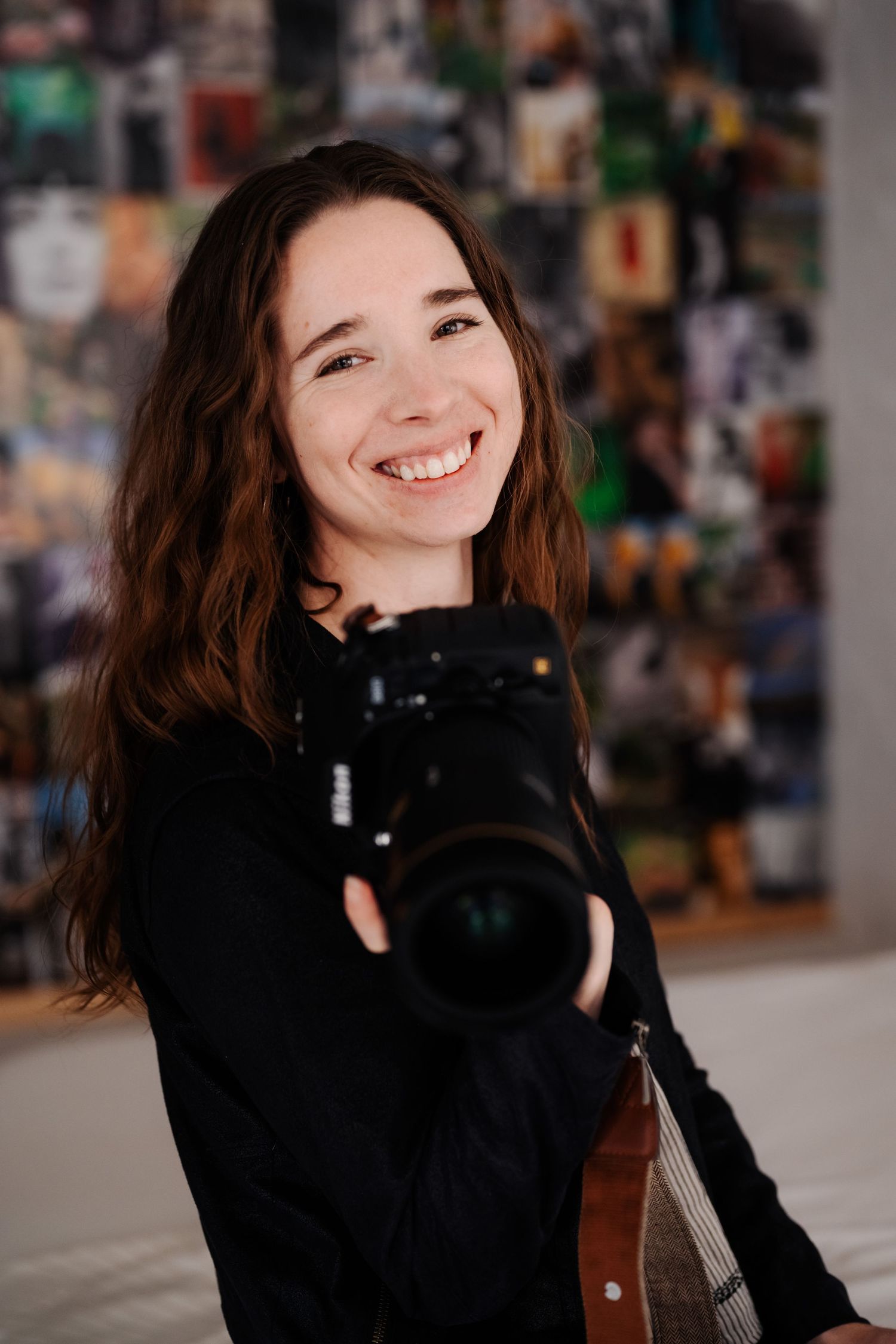 The photographer stands with her camera smiling and looking into the camera.