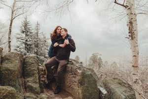 A couple shares an intimate moment while sitting on rocks in a misty winter forest setting.