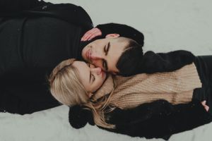An overhead view of a couple lying together on a light background in casual winter wear.