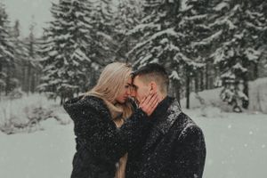 A couple shares an intimate moment in a snow-covered forest landscape.