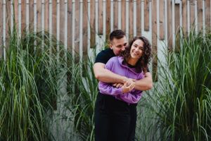 A couple embraces in a field of tall grass during a romantic outdoor photoshoot.