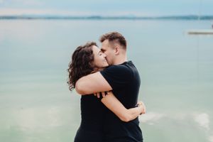 A romantic embrace captured against a serene waterfront background with soft blue tones.