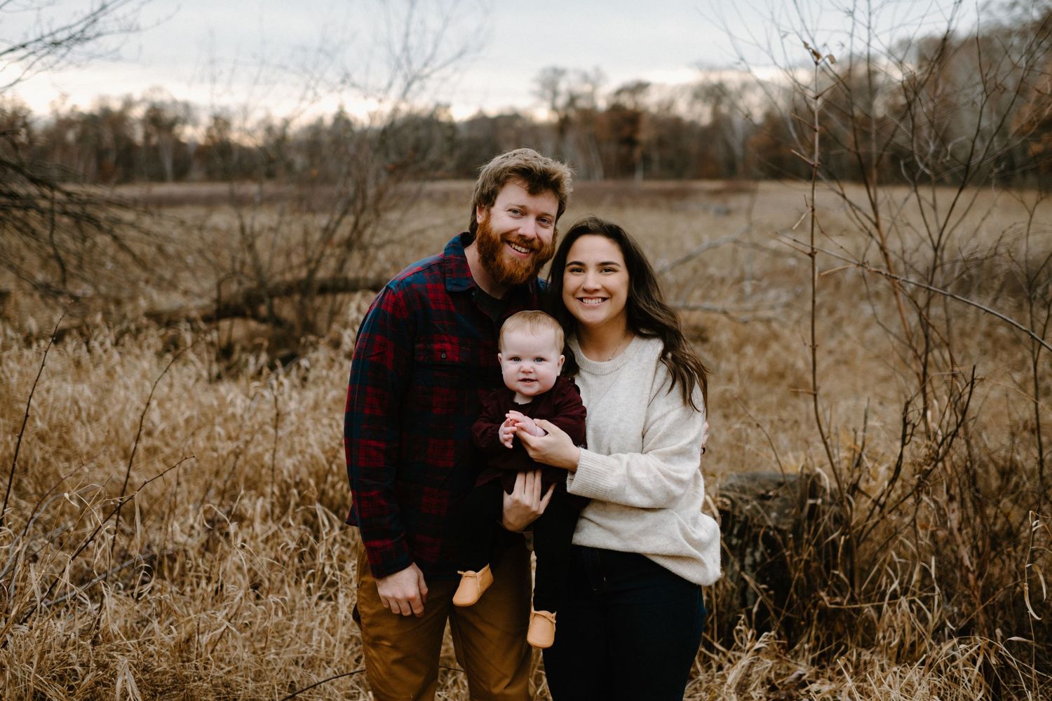 Family portrait in autumn field with tall grass and trees in background.