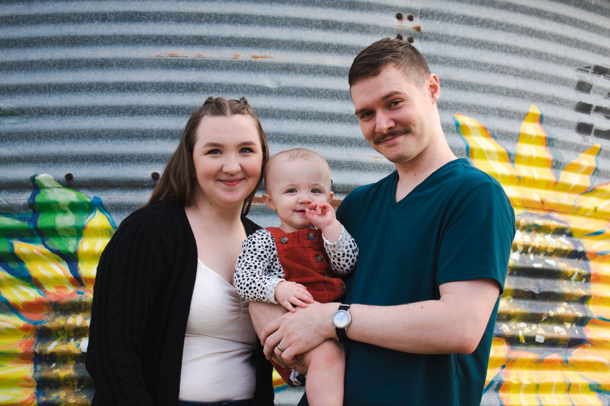 A young family poses at a local pumpkin patch with their baby