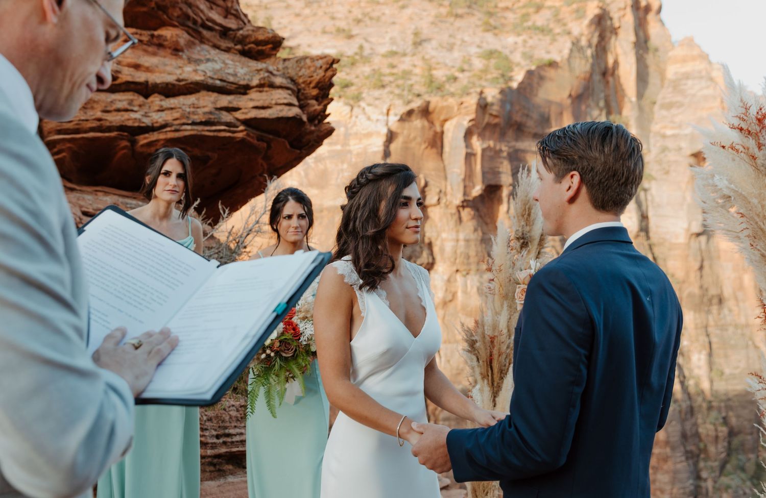 A wedding ceremony takes place against dramatic red rock formations in a desert landscape.