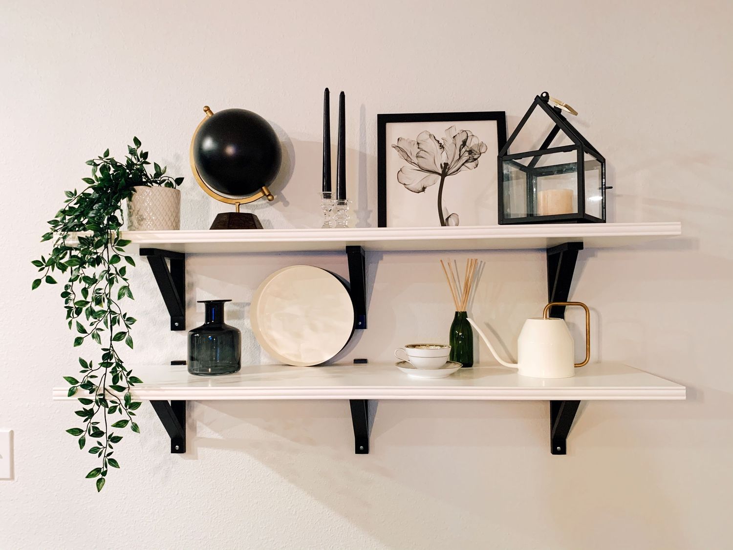 Minimalist white shelving display with black accents, plants and decorative home accessories.
