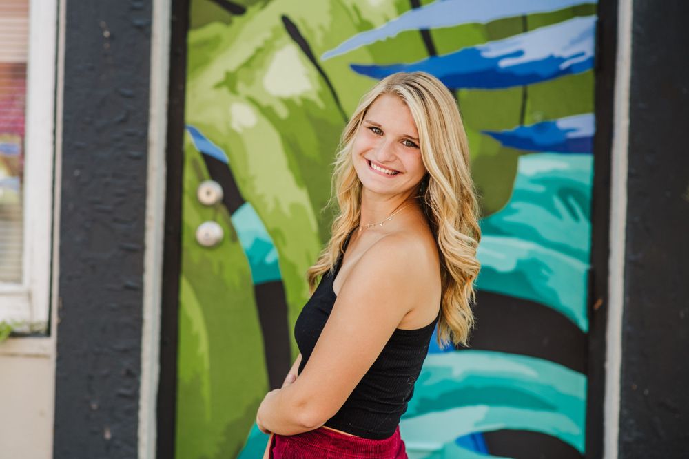 Casual pose against colorful street art wall wearing black tank top.