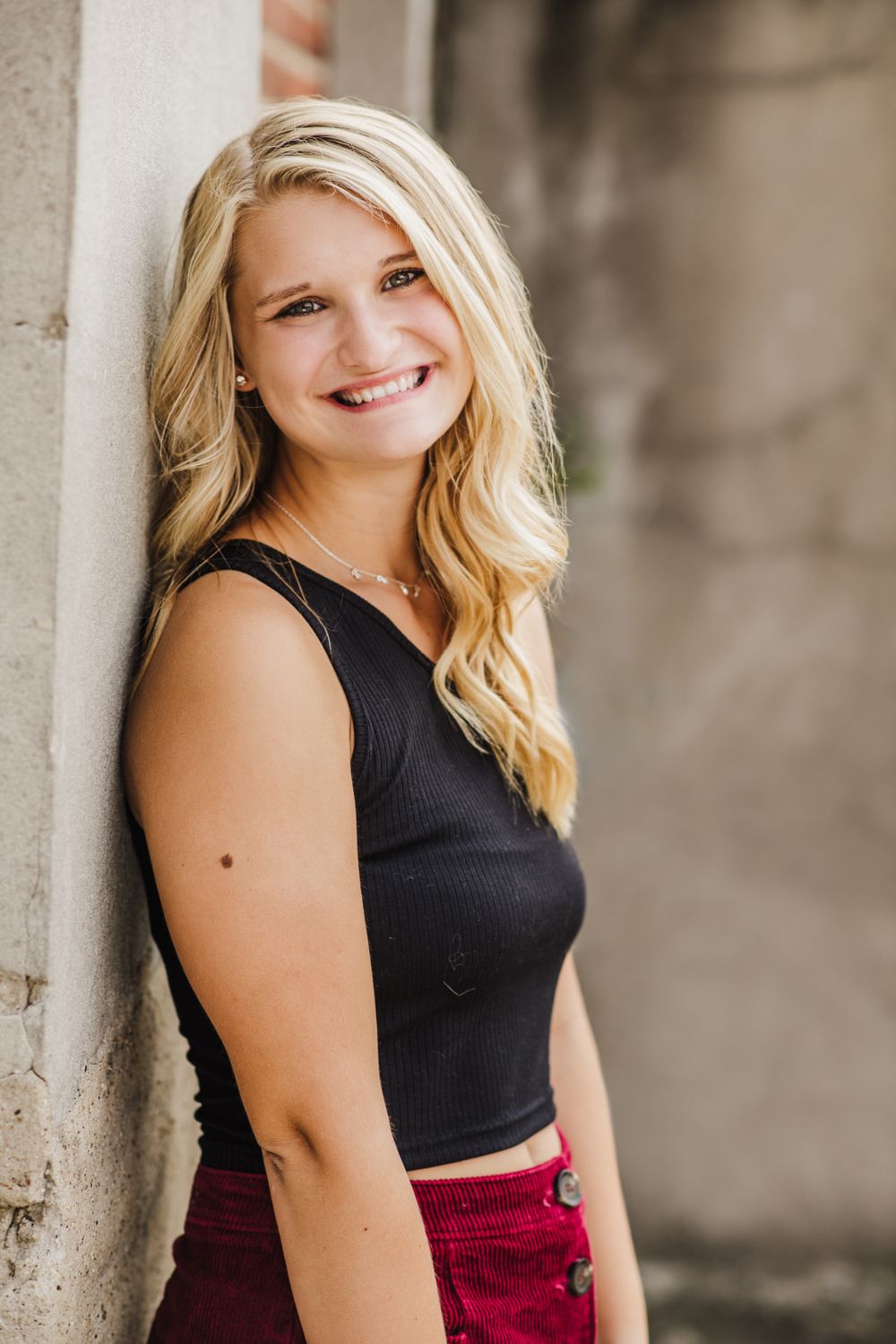 Portrait against neutral wall wearing black sleeveless top and burgundy bottom.
