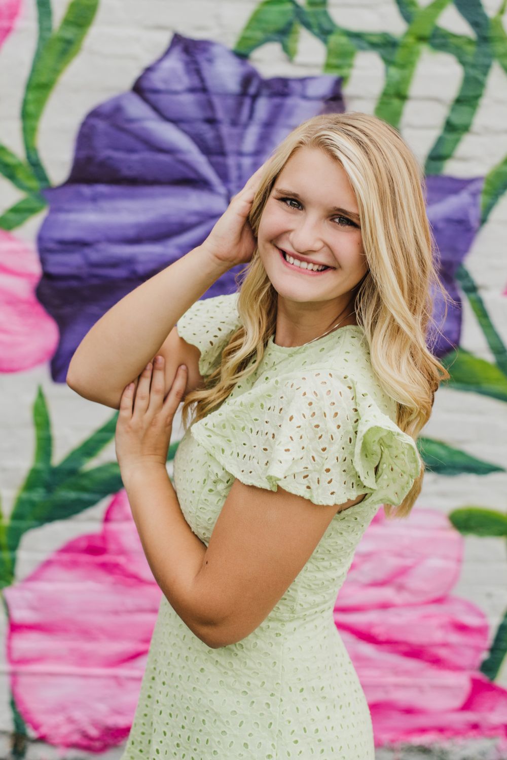 Casual poses against artistic wall mural with floral designs.