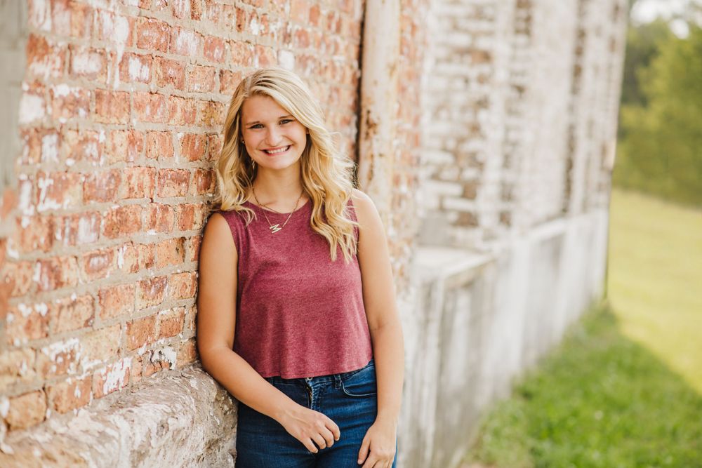 Casual portrait against weathered brick wall wearing burgundy tank top and blue jeans.