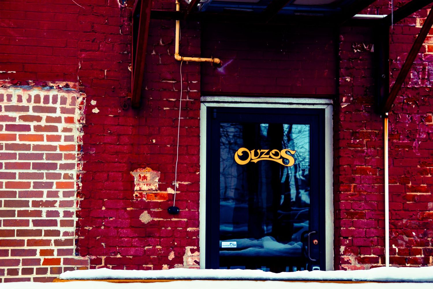 A neon sign glows through a glass door on a red brick building facade.