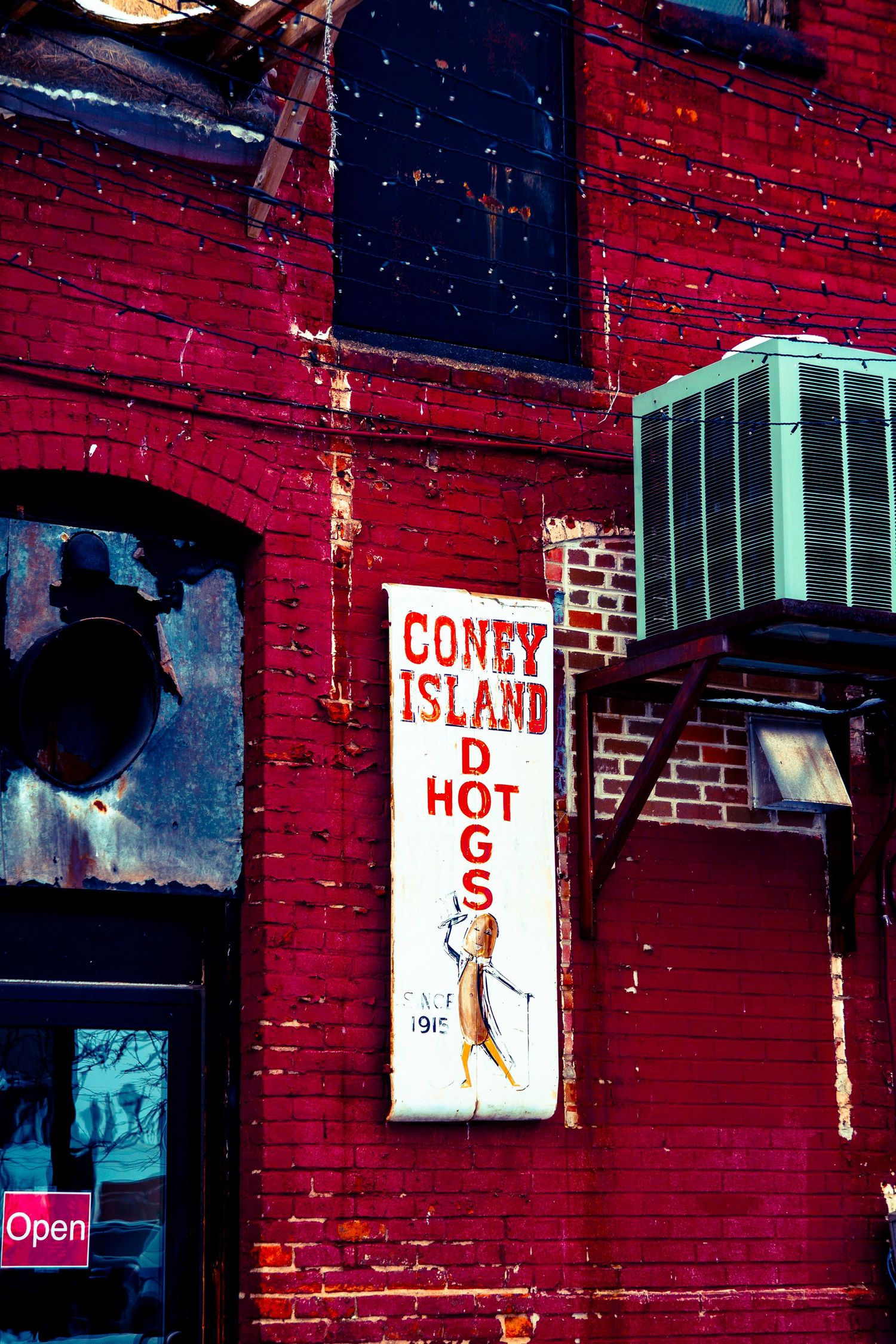 A vintage Coney Island hot dog sign mounted on a weathered red brick wall.
