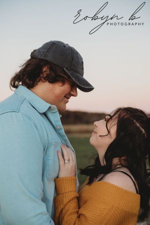 A couple in casual clothing share an intimate moment at sunset, with one wearing a blue shirt and the other in a yellow sweater.
