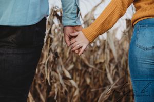 A couple walks hand in hand through a field of dried autumn corn stalks during a fall afternoon.