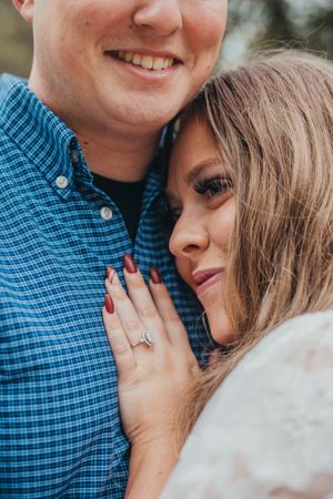 A close-up engagement photo showing a couple embracing, with the woman's hand displaying her new ring.