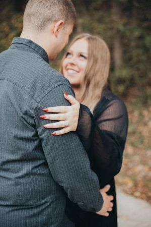 A couple embraces in an outdoor setting, with the woman in a sheer black top showing her red nail polish.