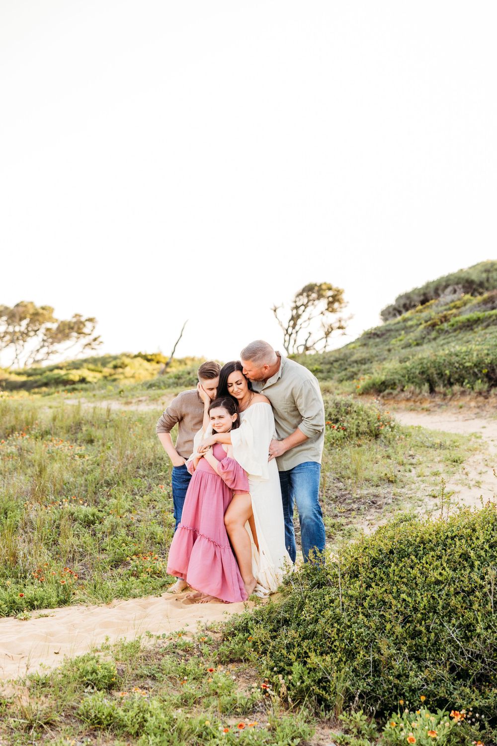 A family shares an intimate moment on a coastal hiking trail during golden hour.