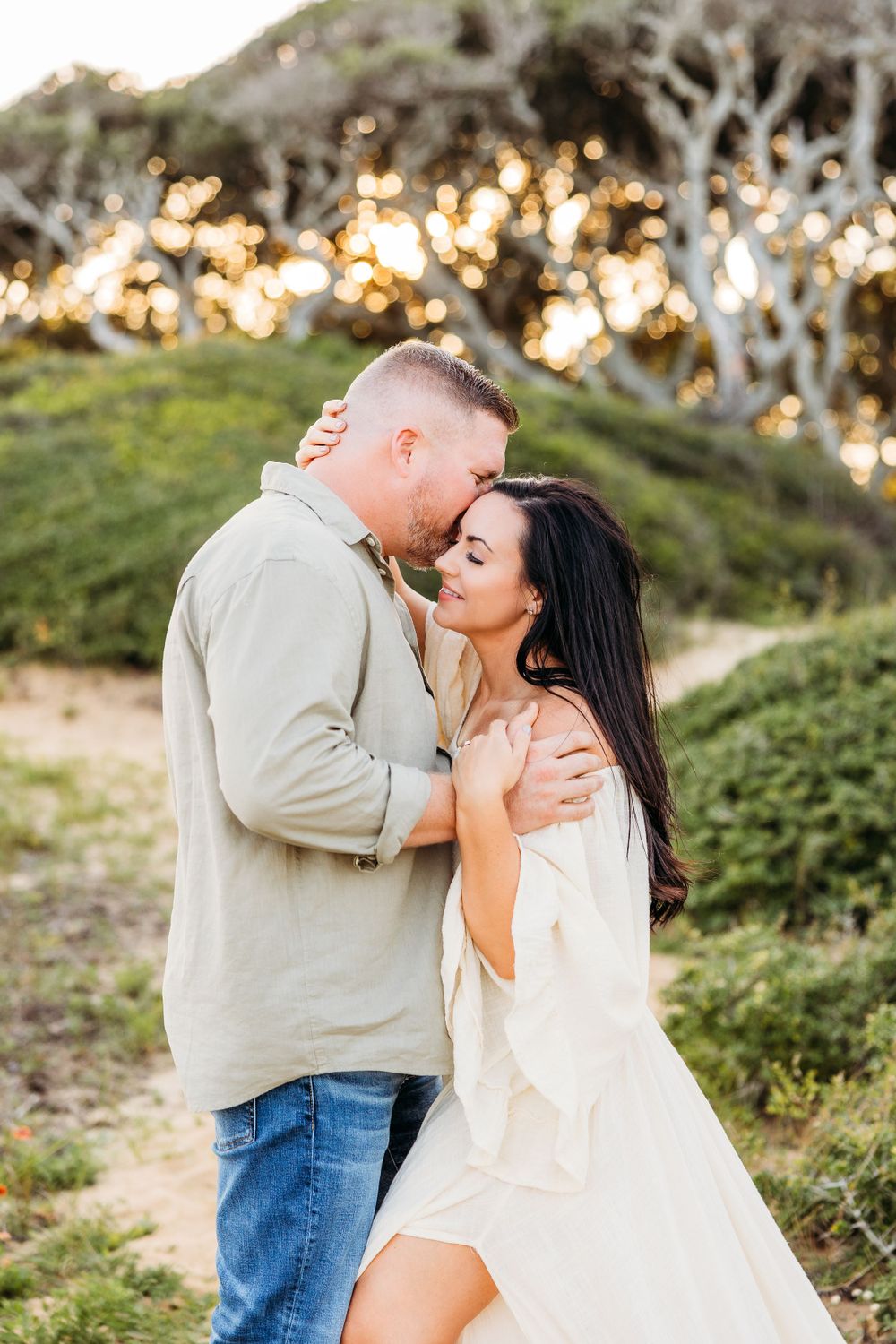 A romantic embrace on a hillside path with golden sunlight filtering through trees.