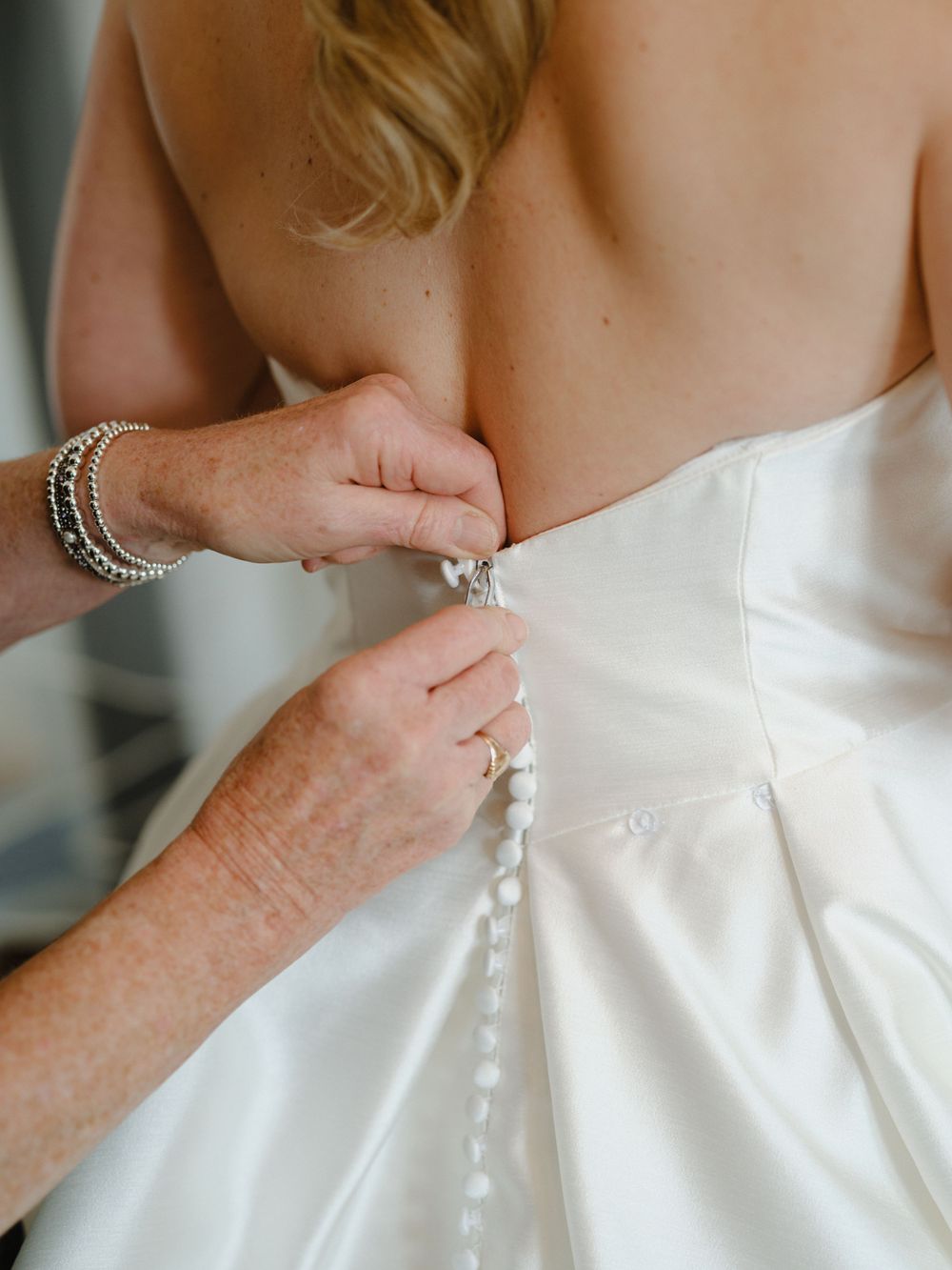 Detail shot of white wedding dress being fastened with pearl buttons.