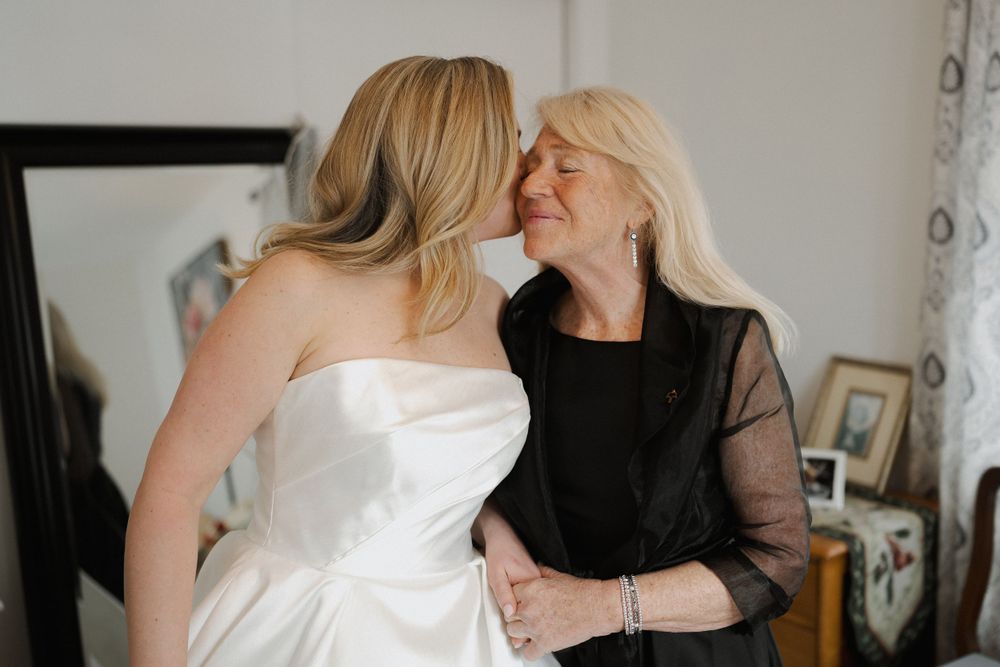 Wedding party wearing black dresses gather around and assist the bride.