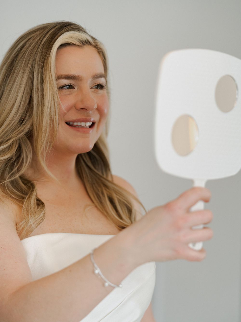 Bride in strapless wedding gown poses elegantly against white background.