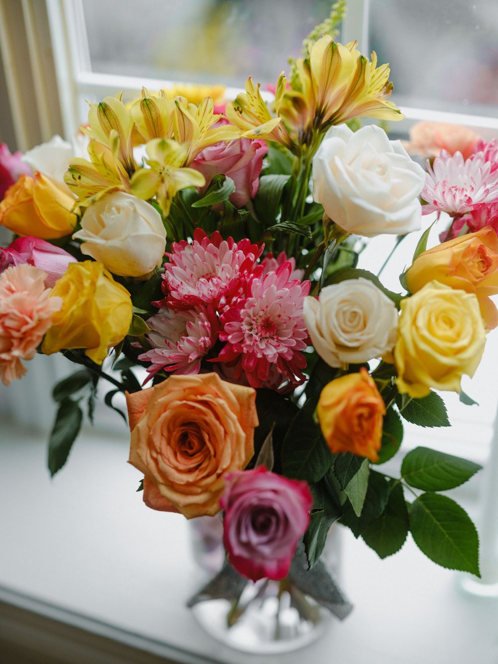 Colorful floral arrangement with roses, carnations and yellow daisies in a clear vase.