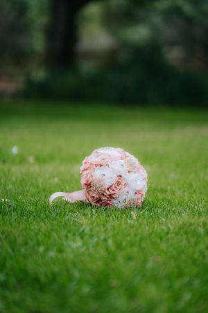 A delicate pink and white rose bouquet rests on green grass in an outdoor setting.