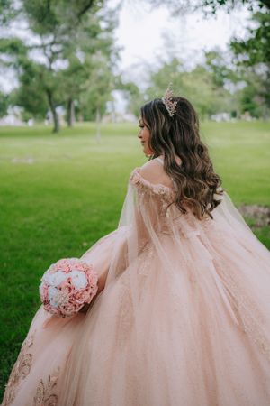 An elegant blush pink ball gown with intricate details photographed from behind in a garden setting.